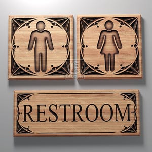 May include: A wooden sign with the word "RESTROOM" in a decorative font. The sign is flanked by two smaller signs, one with a male symbol and the other with a female symbol.
