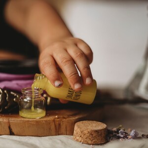 Puede incluir: Una mano vierte l&iacute;quido amarillo de una peque&ntilde;a botella etiquetada como "Snake Venom" en una botella de vidrio transparente.