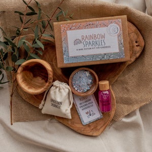 May include: A wooden tray with a small wooden bowl filled with blue and pink glitter, a small pouch with the text "Unicorn Sparkle", a small bottle of pink liquid with the text "Rainbow Sparkle", and a card with the text "Kind like a unicorn spreading magic wherever I go".