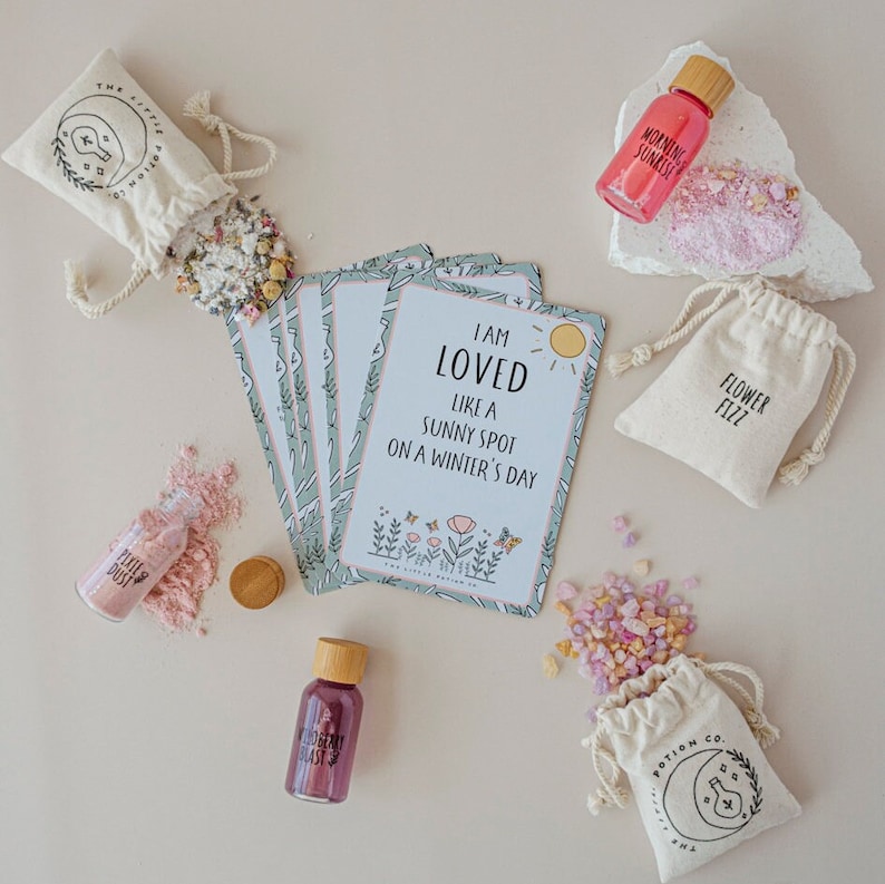 Puede incluir: Un conjunto de productos de ba&ntilde;o con un tema relajante. El conjunto incluye una peque&ntilde;a botella de sales de ba&ntilde;o, una peque&ntilde;a botella de aceite de ba&ntilde;o, una peque&ntilde;a bolsa de bombas de ba&ntilde;o y un juego de tarjetas de afirmaci&oacute;n. Las tarjetas de afirmaci&oacute;n tienen un dise&ntilde;o floral y el texto "Soy amado como un lugar soleado en un d&iacute;a de invierno".