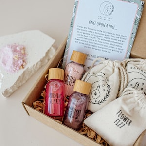 Puede incluir: Una caja de regalo llena de peque&ntilde;as botellas de productos de ba&ntilde;o, incluyendo "Morning Sunrise", "Wildberry Blast" y "Pixie Dust". La caja tambi&eacute;n incluye tres peque&ntilde;as bolsas de muselina etiquetadas como "Potion Co.", "Flower Fizz" y "Potion".
