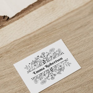 Puede incluir: Una tarjeta blanca con un dise&ntilde;o floral negro y el texto "Emma Robertson" en una pancarta.