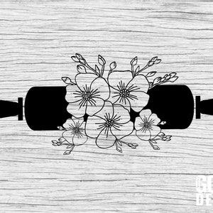 May include: Black and white silhouette of a rolling pin with a floral design. The flowers are stylized and have five petals. The rolling pin is centered on a woodgrain background. The text "God Bless" is at the bottom of the image.