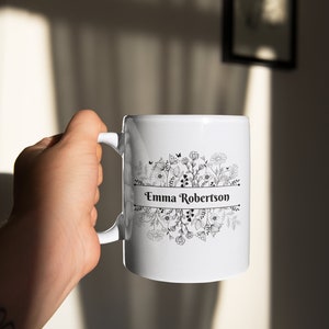 Puede incluir: Taza de cer&aacute;mica blanca con un dise&ntilde;o floral negro y el nombre "Emma Robertson" impreso en una pancarta.