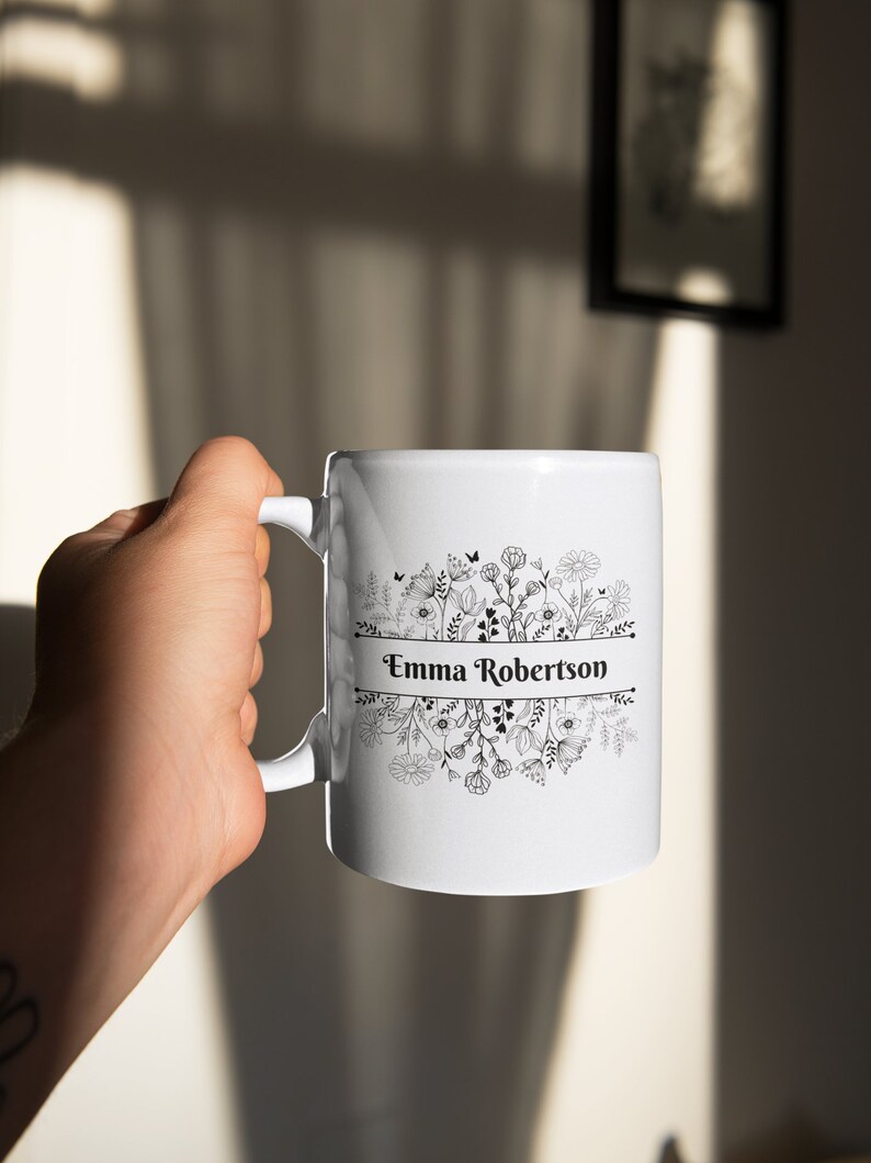 Puede incluir: Taza de cer&aacute;mica blanca con un dise&ntilde;o floral negro y el nombre "Emma Robertson" impreso en una pancarta.
