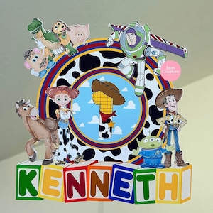 K&ouml;nnte beinhalten: Ein farbenfroher Tortenaufsatz mit Figuren aus dem Film Toy Story. Das Design zeigt Buzz Lightyear, Woody, Jessie und weitere Charaktere. Der Name "KENNETH" ist auf Bl&ouml;cken unten geschrieben, mit der Zahl eins in der Mitte.