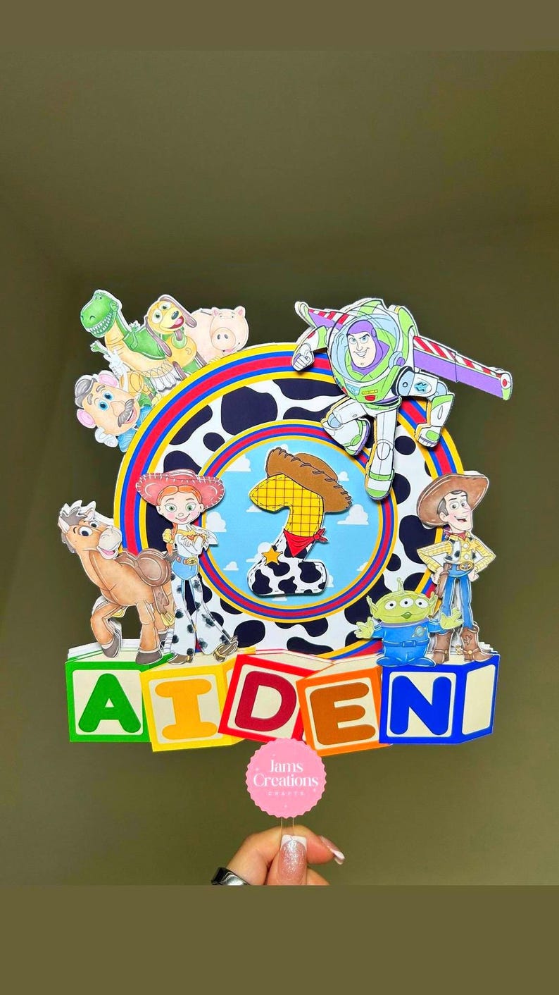 K&ouml;nnte beinhalten: Ein farbenfroher Tortenaufsatz mit Figuren aus dem Film Toy Story, darunter Buzz Lightyear und Woody. Das Design enth&auml;lt den Namen "AIDEN" in bunten Buchstaben. Der Aufsatz befindet sich vor einem gr&uuml;nen Hintergrund mit einem kreisf&ouml;rmigen Design.
