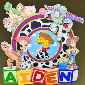 K&ouml;nnte beinhalten: Bunte Tortenaufsatz mit Toy Story-Figuren. Es zeigt Buzz Lightyear, Woody, Jessie und andere, mit dem Namen "AIDEN" in Buchstaben. Das Design umfasst einen Kuhdruck und die Zahl 1. Eine lustige Dekoration f&uuml;r einen Geburtstag.