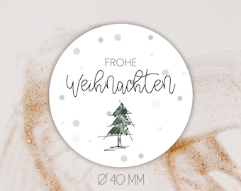 May include: White round sticker with the text "Frohe Weihnachten" in black script. A simple black and green line drawing of a Christmas tree is in the center of the sticker. The sticker has a diameter of 40 mm.