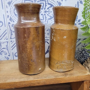 May include: Two brown ceramic stoneware bottles with a rounded bottom and a wide mouth. The bottle on the right has the text "HOLLIS & SONS 14 OLD STREET LONDON" printed on the side.