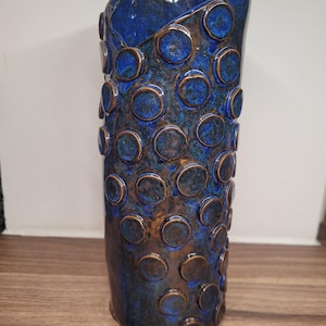 Könnte beinhalten: Eine blaue Keramikvase mit einer strukturierten Oberfläche. Die Vase ist mit einem Muster aus erhabenen Kreisen verziert.