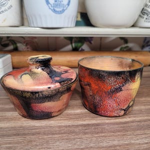 May include: Two small ceramic containers with lids. Both containers have a black, orange, and yellow marbled design.