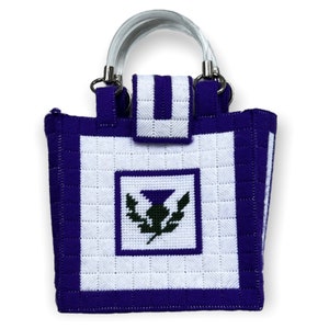 May include: A white tote bag with a purple trim and a purple thistle embroidered on the front. The bag has clear plastic handles.