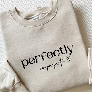 May include: A beige sweatshirt with the text "perfectly imperfect" in black lettering with a small heart symbol.