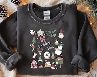 May include: Dark gray sweatshirt with a festive Christmas design. The design includes a Christmas tree, Santa Claus, a snowman, and the words "Christmas Vibes". The sweatshirt is made of a soft material.