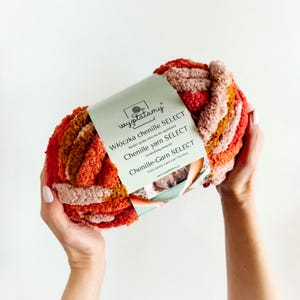 Può includere: Un gomitolo di filato chenille in tonalità arancio, rosa e marrone. Il filato è etichettato con "Włóczka chenille SELECT" e "Chenille yarn SELECT".