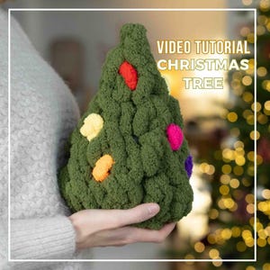 Könnte beinhalten: Ein grüner Weihnachtsbaum aus Garn mit bunten Bommeln als Dekoration. Der Baum wird in der Hand einer Person gehalten. Der Text "VIDEO TUTORIAL CHRISTMAS TREE" wird über dem Baum angezeigt.