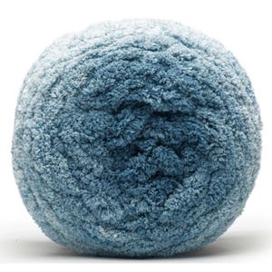 Może przedstawiać: Kłębek miękkiej, teksturowanej przędzy w odcieniach niebieskiego. Przędza wydaje się być wykonana z chenille lub podobnego pluszowego materiału, idealnego do projektów dziewiarskich lub szydełkowych. Kolor przechodzi od jaśniejszego niebieskiego u góry do ciemniejszego niebieskiego u podstawy.