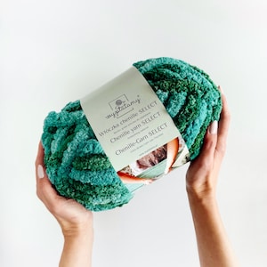 May include: A skein of green and teal chenille yarn. The yarn is soft and fluffy, and it is perfect for making blankets, scarves, and other cozy items. The label reads "Włóczka chenille SELECT" and "Chenille yarn SELECT".