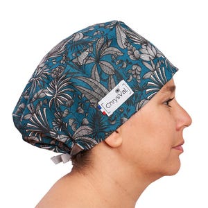 Può includere: Cuffia chirurgica con motivo botanico teal e grigio. La cuffia presenta un'etichetta bianca con la scritta "ChrysVal" e una piccola bandiera francese. La cuffia è legata sul retro.
