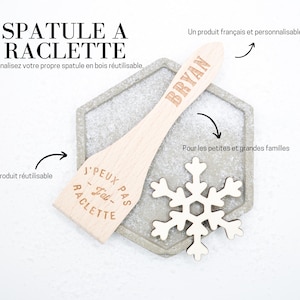 Könnte beinhalten: Ein Holzspatel mit dem Text "J'PEUX PAS - J'ai - RACLETTE" und dem Namen "BRYAN" eingraviert. Der Spatel liegt auf einer grauen sechseckigen Oberfläche mit einer Holzschneeflocke.
