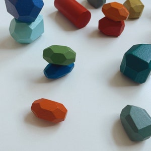 Puede incluir: Un conjunto de formas geométricas de madera de colores, que incluyen una pirámide, un cilindro y varias formas irregulares. Las formas son en tonos de azul, verde, rojo y naranja.