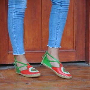 Puede incluir: Zapatos de cuero rojo y verde con un diseño de tiras cruzadas y un patrón decorativo en la punta. Los zapatos están atados con cordones verdes.