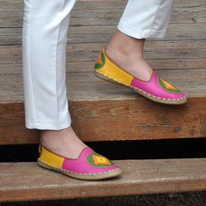 May include: A pair of pink and yellow embroidered slip-on shoes with a jute sole.