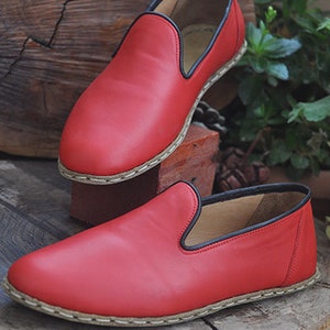 May include: Two pairs of red leather slip-on shoes with black trim and a white stitching detail around the sole.
