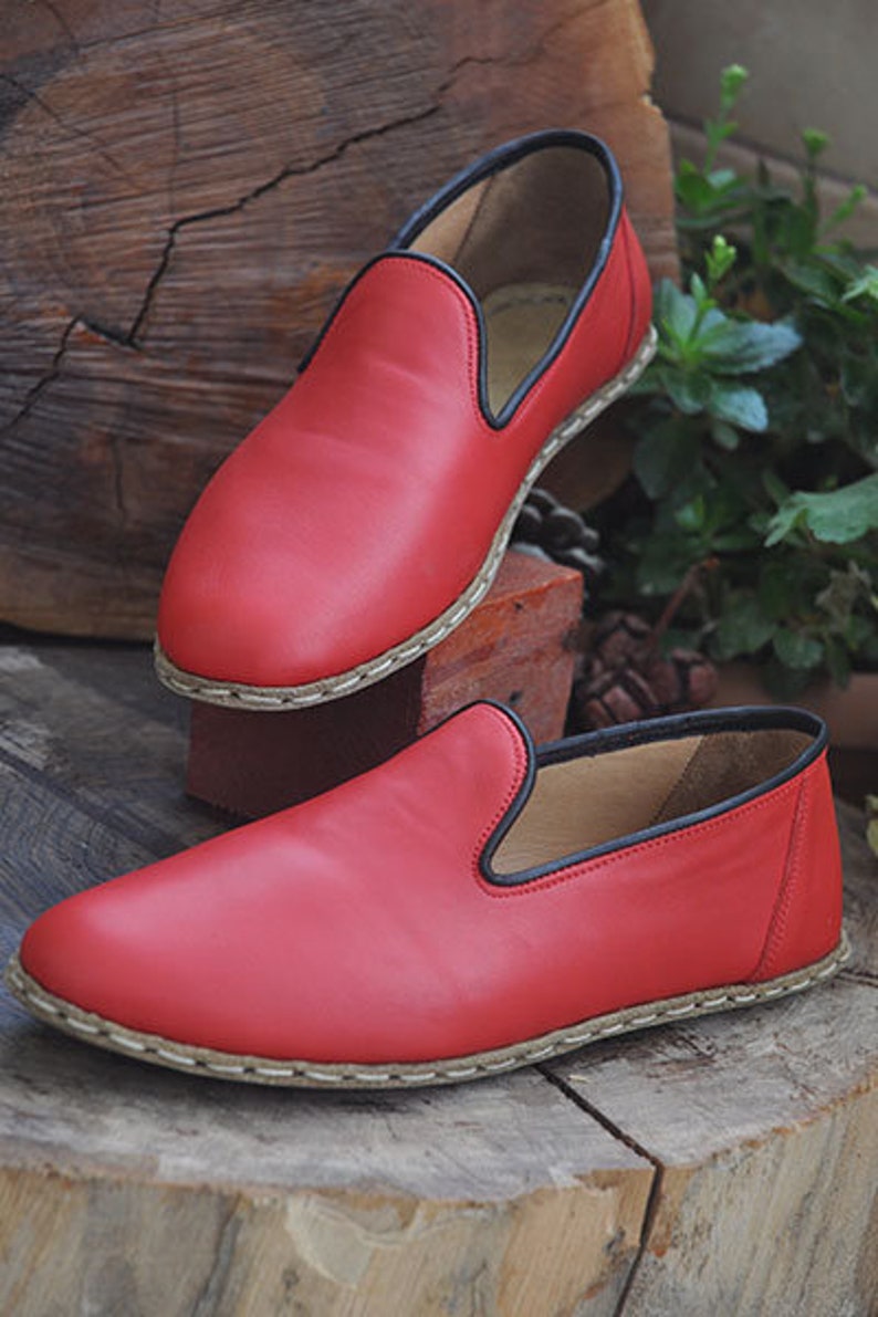 May include: Two pairs of red leather slip-on shoes with black trim and a white stitching detail around the sole.