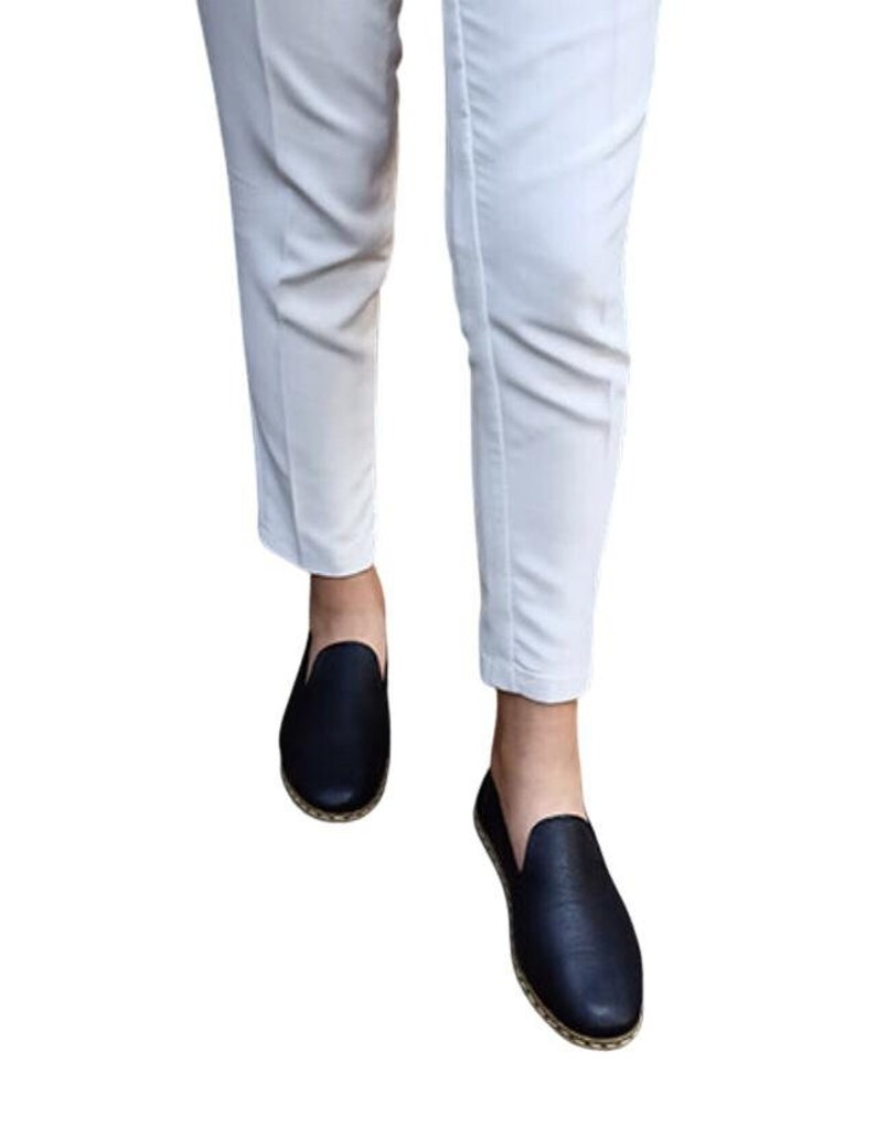 May include: A pair of black leather slip-on shoes with a white stitched trim around the sole.