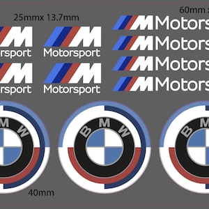 Puede incluir: Una hoja de calcomanías con logotipos y emblemas de BMW Motorsport. La hoja incluye múltiples versiones del logotipo "M" en rojo, azul y blanco, junto con emblemas circulares. Las dimensiones son 2,5 cm x 1,4 cm, 6 cm x 0,7 cm y 4 cm.