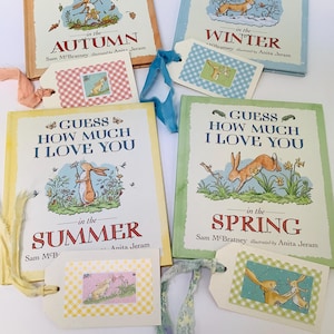 May include: Four children's books titled "Guess How Much I Love You" with seasonal themes: Autumn, Winter, Summer, and Spring. Each book features illustrations of rabbits and coordinating gift tags with ribbon. The books are by Sam McBratney, illustrated by Anita Jeram.