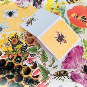 May include: A collection of bee-themed stickers and paper cutouts featuring various bumblebees, honeybees, and floral illustrations. The set includes images of bees on honeycomb, sunflowers, tulips, and pink flowers, alongside a folded yellow card.