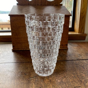 May include: A clear glass vase with a geometric pattern. The vase is tall and slender, with a wide mouth and a narrow base.
