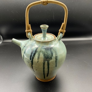 May include: A blue and white ceramic teapot with a bamboo handle. The teapot has a unique glaze with black streaks and a cork base.