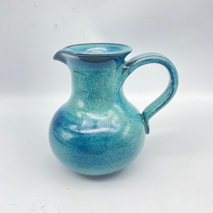 May include: A blue ceramic pitcher with a speckled glaze. The pitcher has a rounded body and a curved handle.