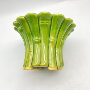 May include: Green ceramic planter shaped like bamboo stalks. The planter has a wide, shallow top and a narrow base with three feet.