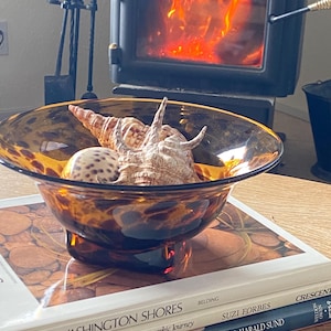 May include: A brown and gold decorative bowl with a seashell inside. The bowl is sitting on top of three books with the text "Washington Shores", "Pacific Northwest", and "A Photographic Journey" on the covers.