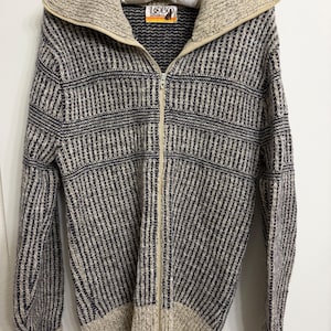 May include: A zip-up knit sweater featuring a textured pattern of navy blue and beige vertical stripes. The garment has a wide, fold-over collar, long sleeves with ribbed cuffs, and a full-length front zipper. A label reading LOBO is at the neck.