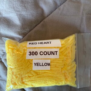 Könnte beinhalten: Eine durchsichtige Plastiktüte gefüllt mit gelbem Garn. Das Etikett lautet "Red Heart 300 Count Yellow."