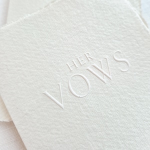 May include: Off-white textured paper with the embossed words "HER VOWS" in a delicate, sans-serif font. The paper has a soft, natural appearance, suggesting a handmade or artisanal quality. The overall aesthetic is minimalist and elegant.
