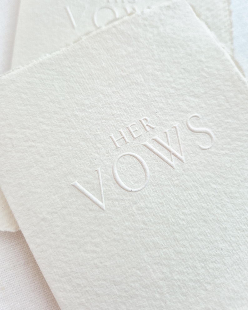 May include: Off-white textured paper with the embossed words "HER VOWS" in a delicate, sans-serif font. The paper has a soft, natural appearance, suggesting a handmade or artisanal quality. The overall aesthetic is minimalist and elegant.