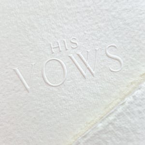 May include: Close-up of a textured, off-white paper with the embossed words "HIS VOWS". The paper has a deckled edge and a subtle, natural appearance, perfect for wedding stationery.
