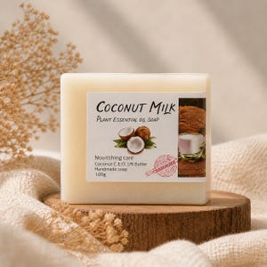 May include: A square bar of handmade coconut milk soap with a label featuring text and images of coconuts. The label reads "Coconut Milk Plant Essential Oil Soap" and "Nourishing care". The soap is displayed on a wooden surface.