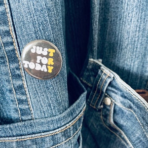 Peut inclure: Un bouton argenté avec les mots "JUST FOR TODAY" en lettres jaunes sur un fond en jean bleu.