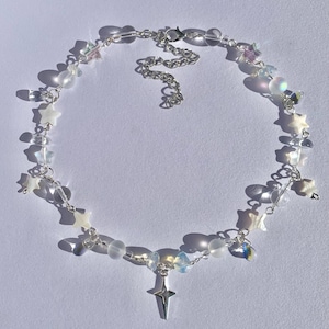 May include: A delicate silver chain necklace with a star charm and iridescent beads. The necklace features a variety of star-shaped charms and clear and opaque beads.