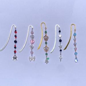 Puede incluir: Cinco marcadores de metal decorativos con abalorios de cuentas. Los abalorios incluyen cuentas de varios colores, corazones, estrellas, flores y una araña. Los marcadores tienen acabados plateados y dorados.