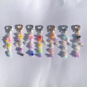 Puede incluir: Seis llaveros con cuentas y cierres en forma de corazón. Cada dije presenta una combinación de colores diferente, incluyendo arcoíris, pastel y tonos joya. Los dijes están adornados con cuentas y detalles en forma de estrella.