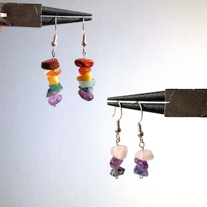 May include: A pair of silver earrings with stacked gemstone charms. The earrings feature a rainbow of colours, including red, orange, yellow, green, blue, and purple. The bottom pair of earrings feature pink, purple, and blue gemstones.